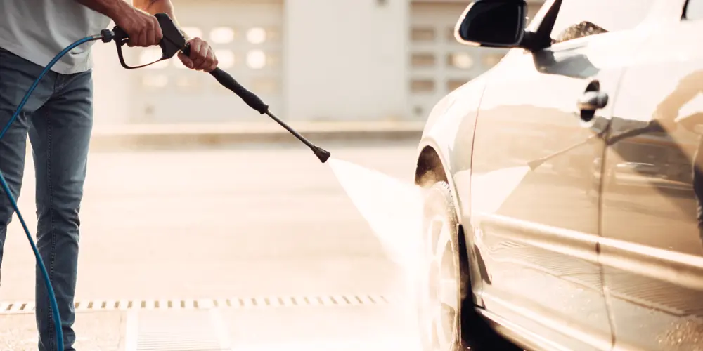 Мужчина моет автомобиль с помощью мини-мойки.