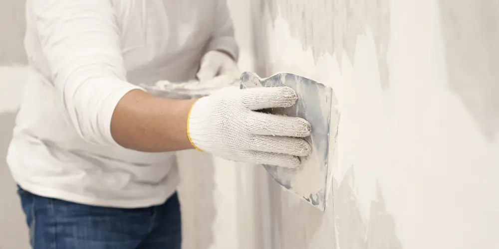 Мужчина шпатлюет стену.