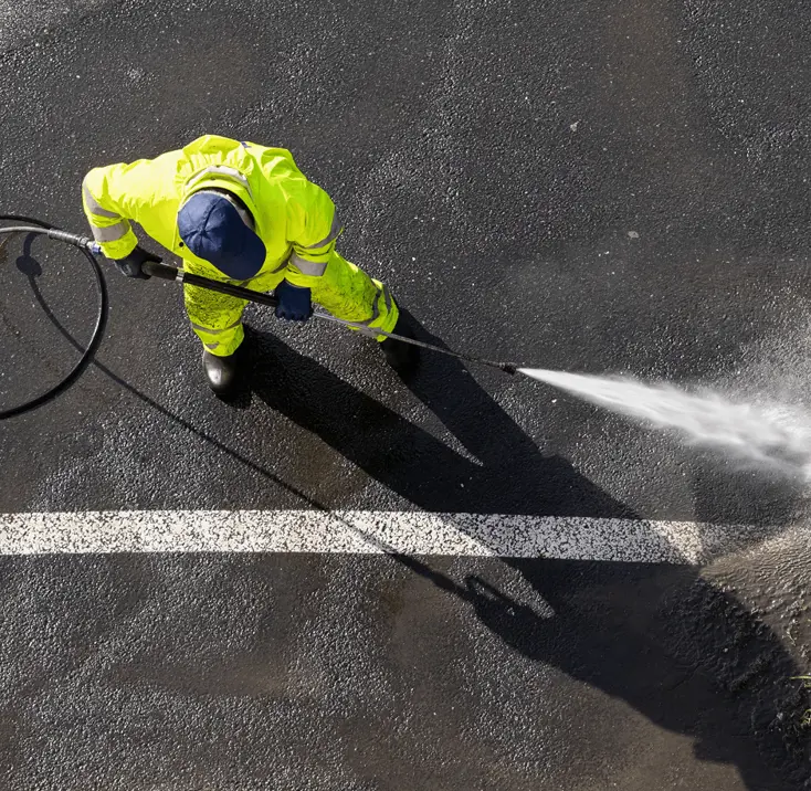 Рабочий моет асфальт струёй воды.
